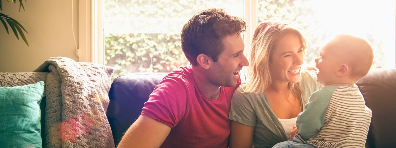 Couple with baby sitting on couch next to window