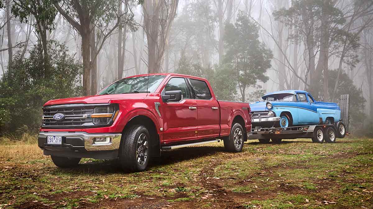 Red Ford F-150 XLT pick-up towing blue vintage car on trailer in misty high country location.