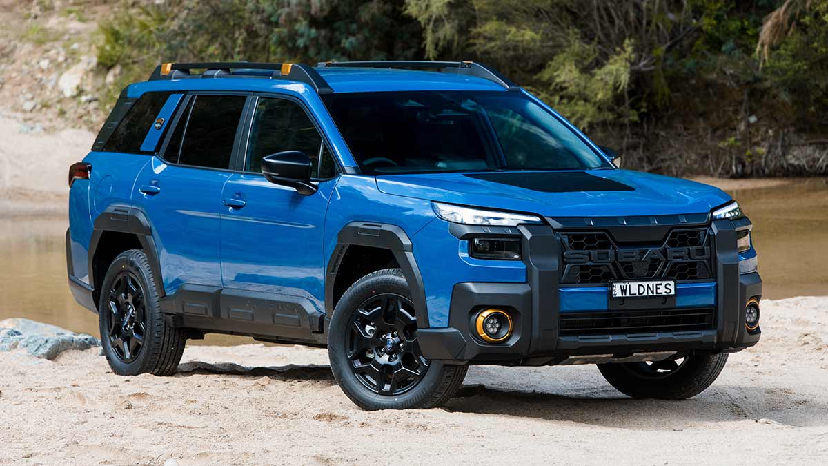 Blue Subaru Outback Wilderness parked on bank of sandy creek.