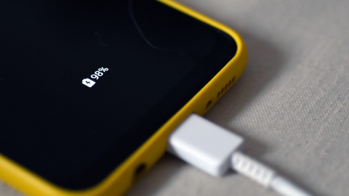 smartphone in a yellow case plugged in and charging; battery reads 98 per cent