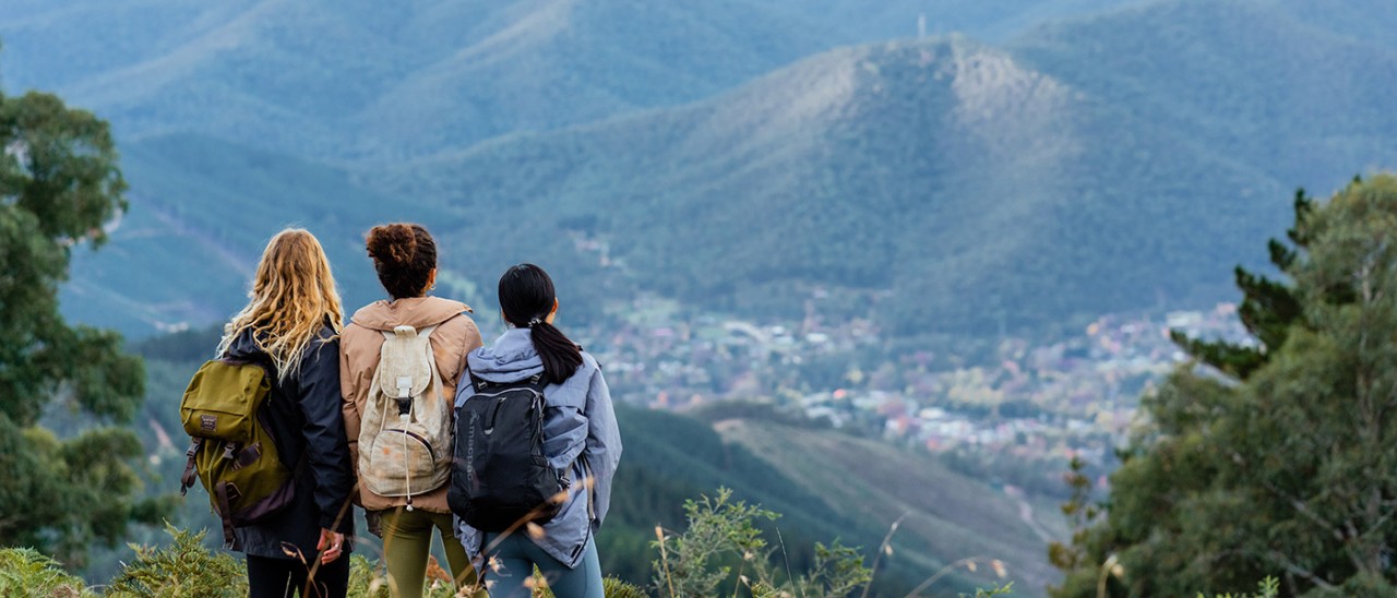 Three hikers with panoramic view of town of Bright and Victorian Alps.