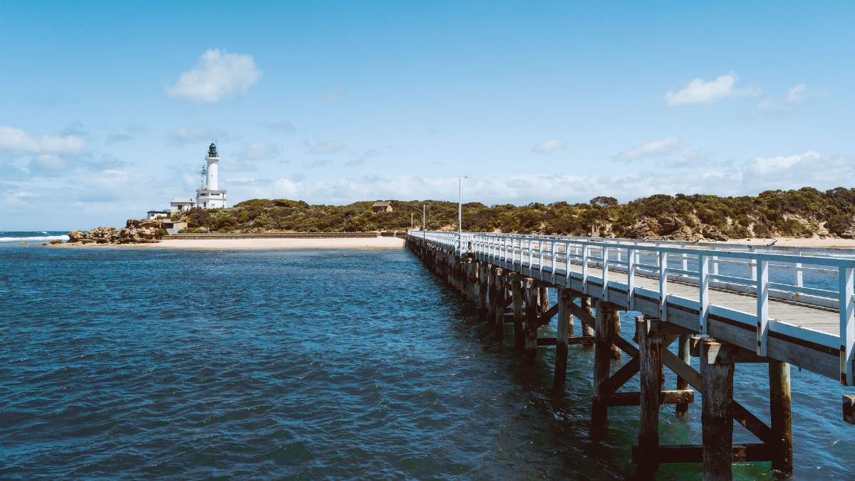 ocean pier with lighthouse on headland in background