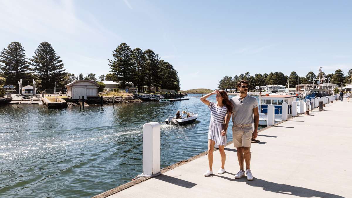 couple walking along Port Fairy harbour with boat in water