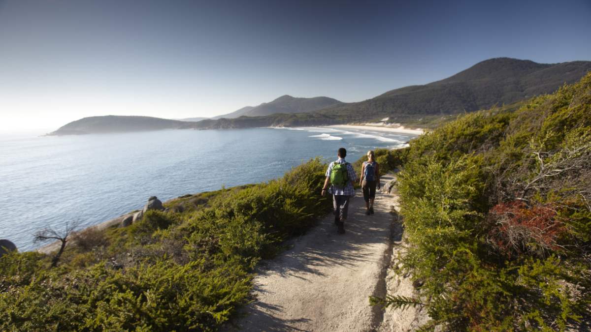 young man and woman walking along a sandy track by the ocean