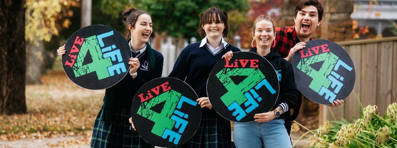 Four young people smiling while holding up circular 'Live4Life' signs