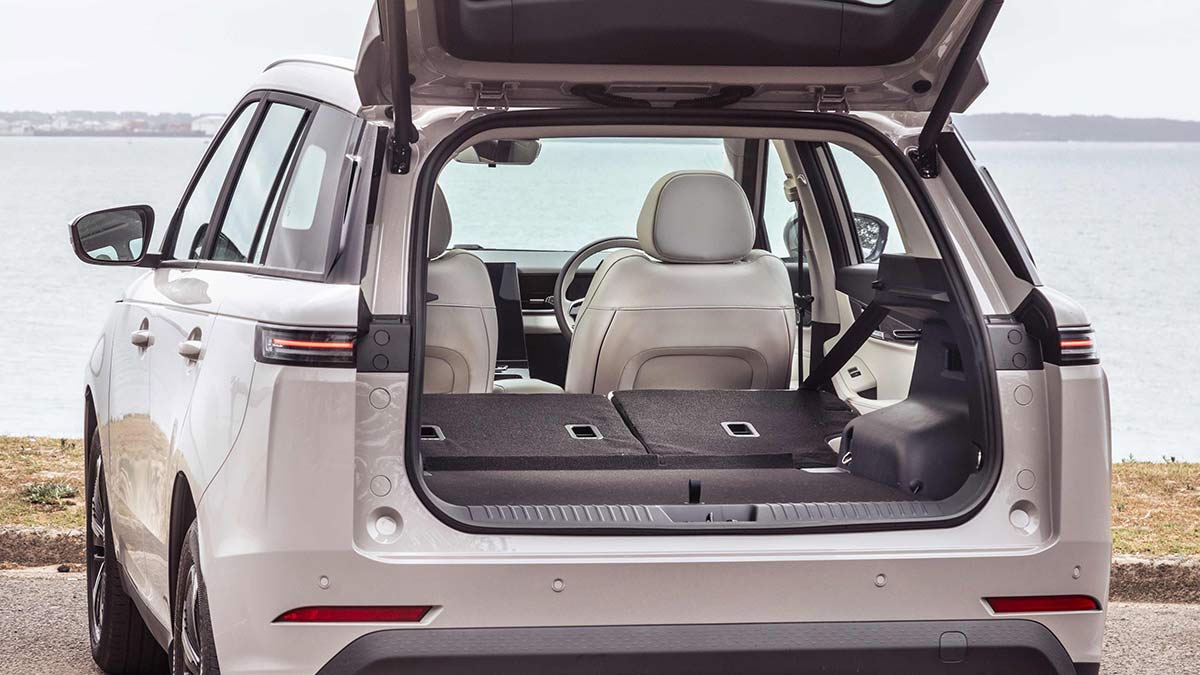 White Jaecoo J5 EV at beachfront carpark with tailgate open, showing cargo area and rear seats folded.