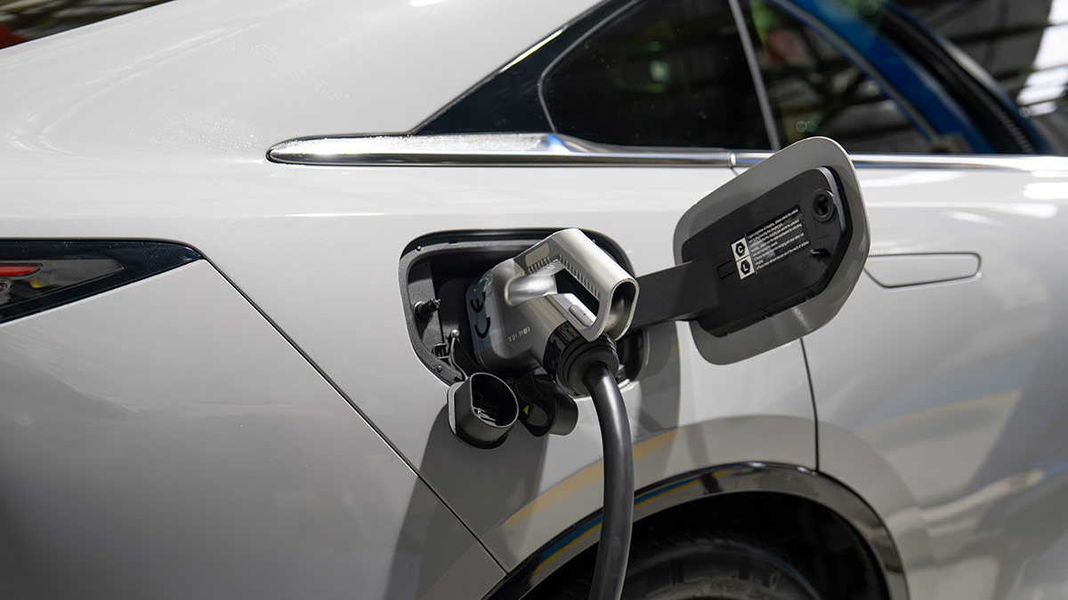 Charging cover open on right rear flank of light grey Mazda 6e EV with CCS2 plug in socket for DC rapid charging.