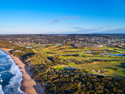 Aerial view of RACV Torquay resort with lush green grasses and the edge of the ocean.