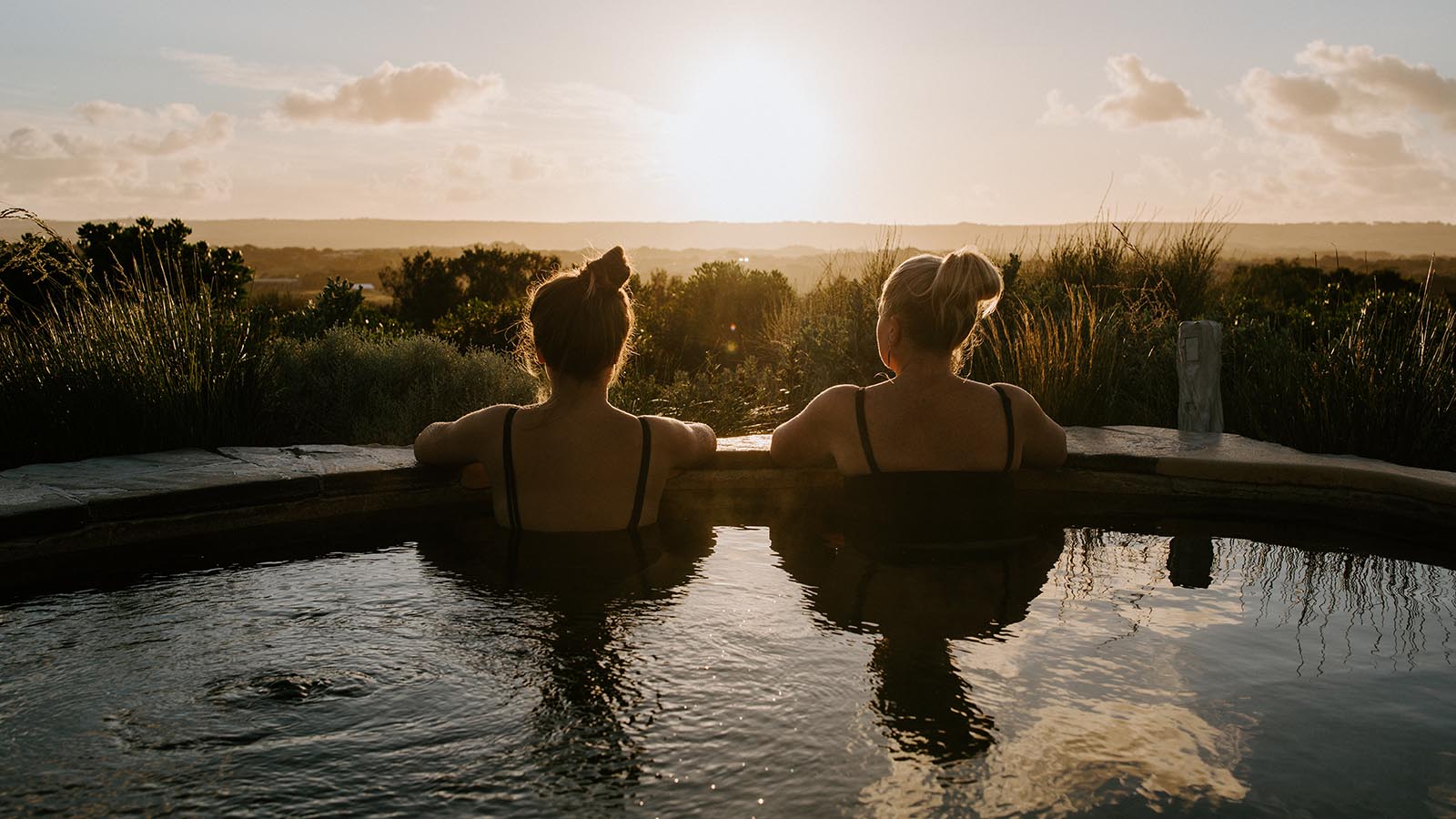 Two women looking over the edge of an outdoor bath at the peninsula landscape.