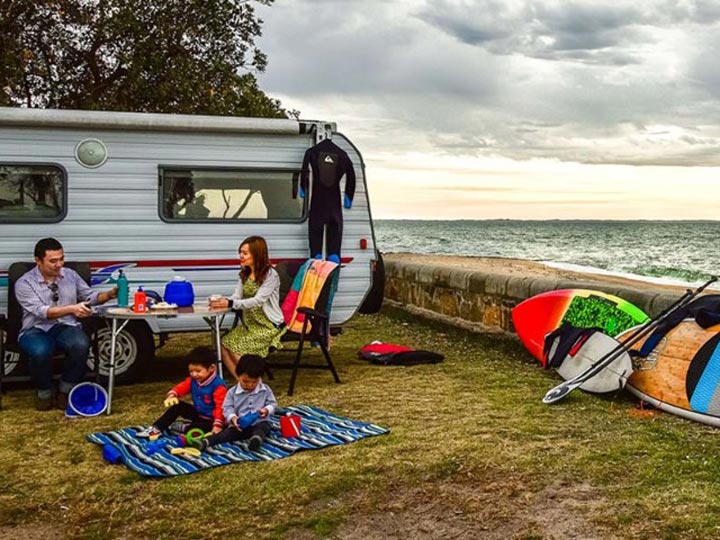 Young family sitting outside of a caravan next to the beach.