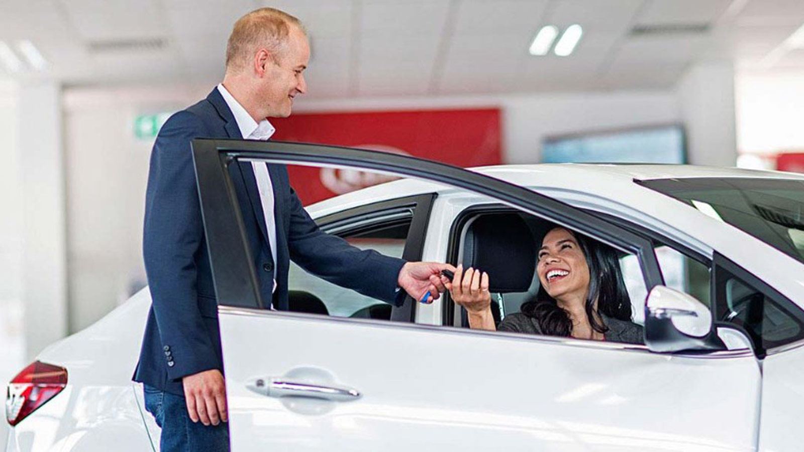 Car salesman handing the keys to a woman sitting in a Kia.