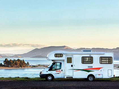 Campervan parked near the beach, water and hills visible in the distance.
