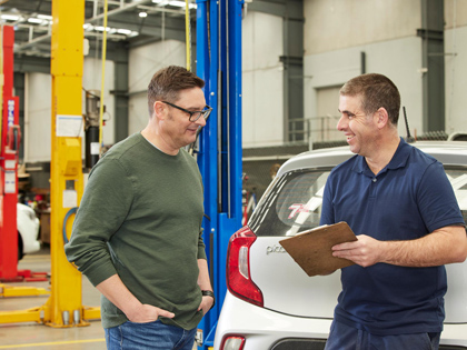 Mechanic with a clipboard smiling at a customer in a workshop.
