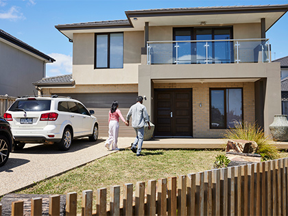 Couple holding hands and walking into a double storey house.