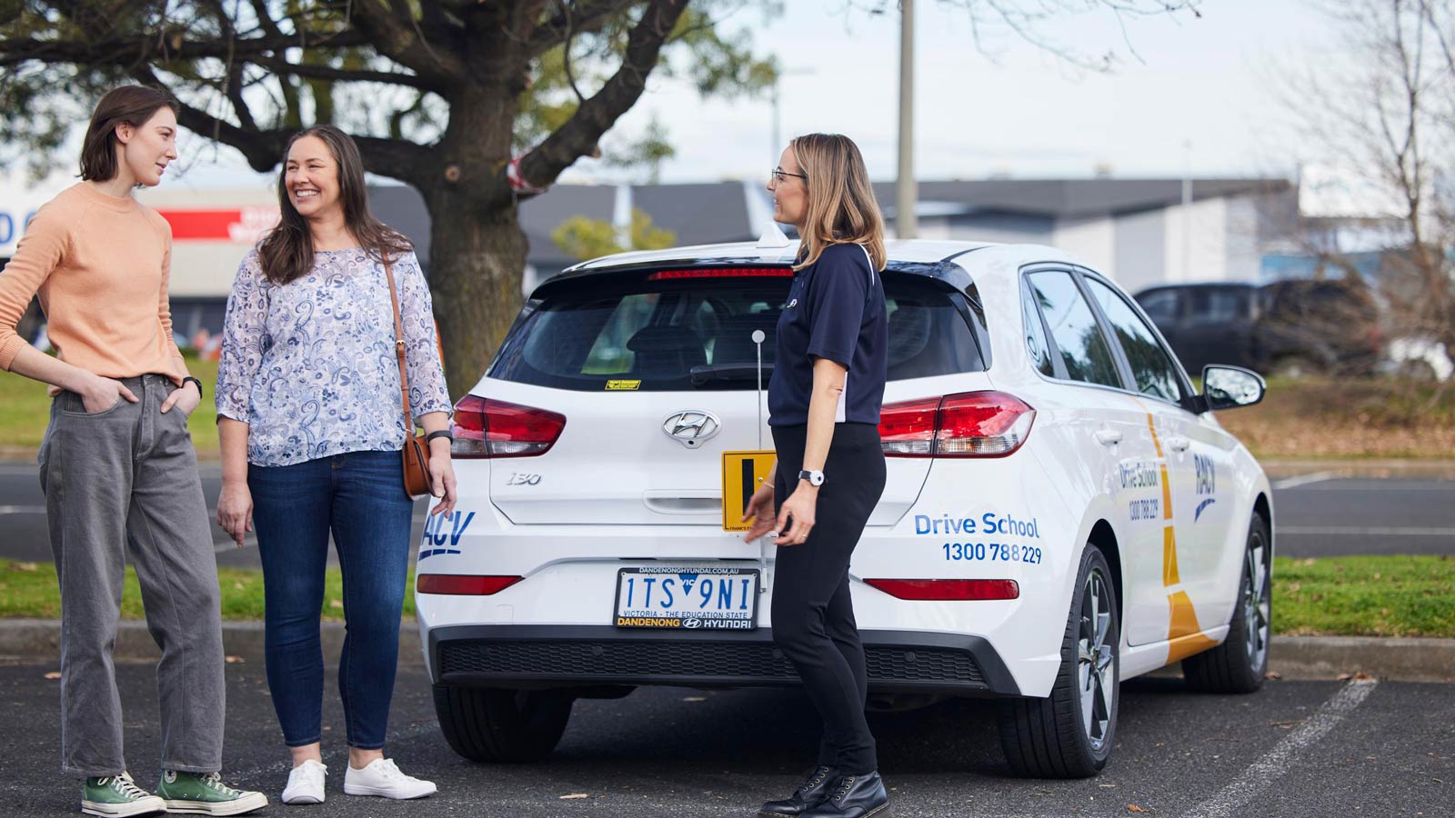 Learner and their mother speaking with a driving instructor standing next to a practice vehicle.