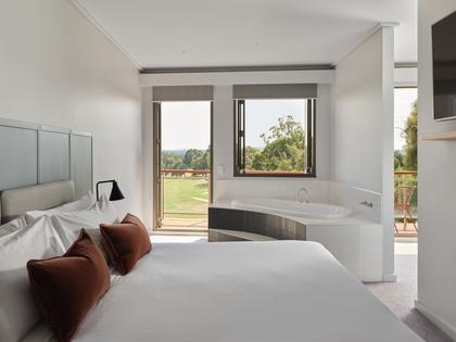Goldfields premium fairway suite features a bed, a wall-mounted TV, two windows, and a corner bathtub.