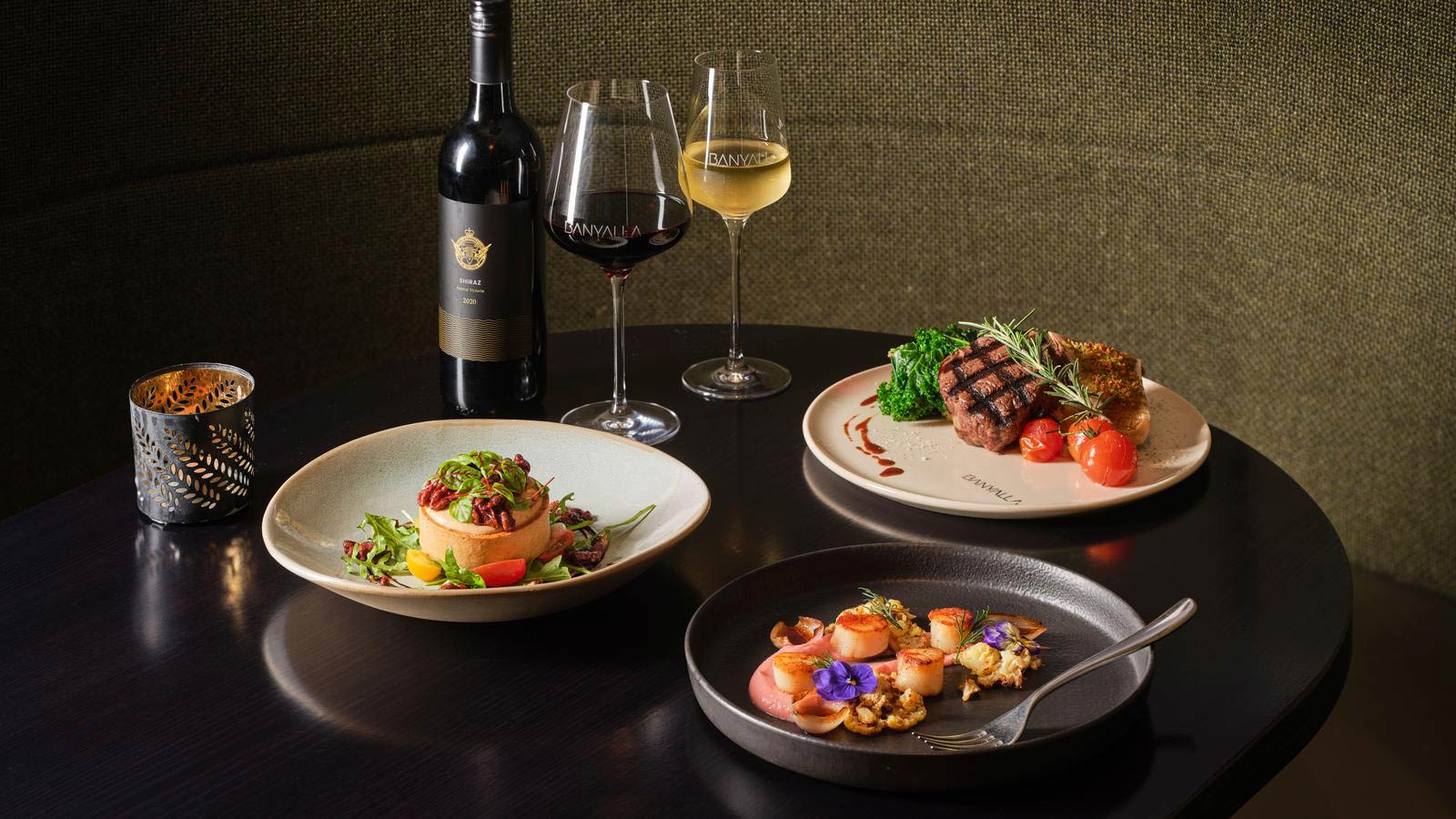 Three different dishes and two filled wine glasses with wine bottle at Banyalla restaurant at RACV Healesville Country Club and Resort.