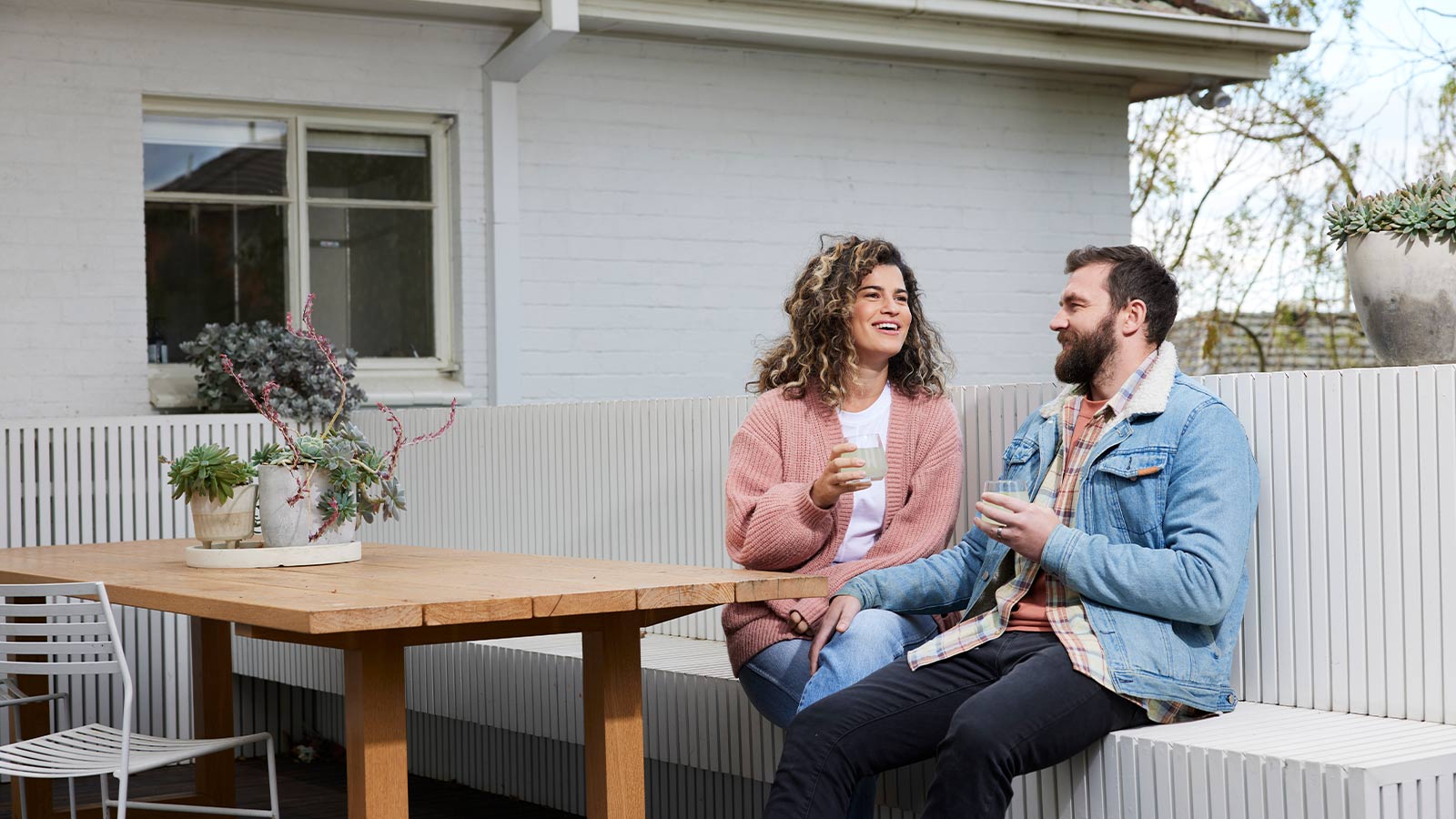 A couple sitting together outside their house, holding drinks and smiling.
