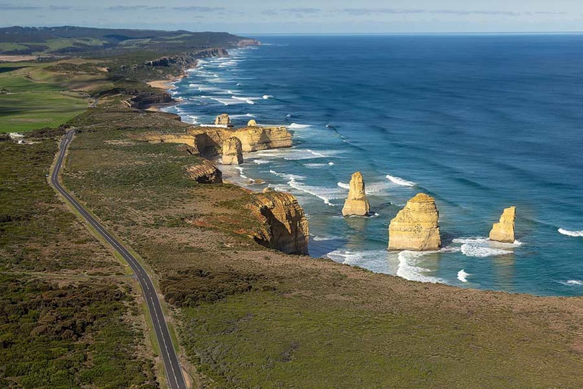 Aerial view of Twelve Apostles with Great Ocean Road alongside and ocean views and coastline into distance