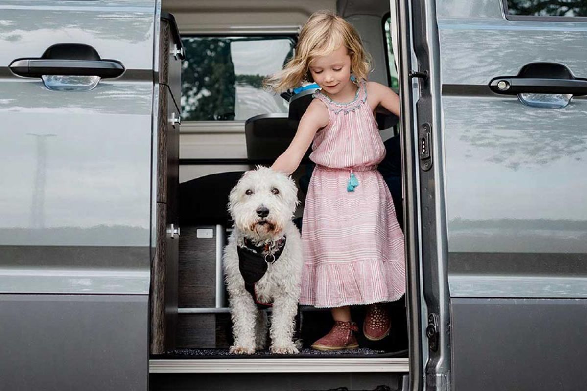 Little girl in a pink dress getting out of a caravan with a fluffy white dog