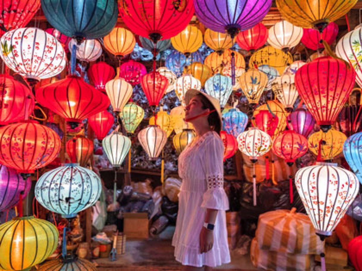 A woman wearing a rice hat in a shop admiring the colourful lanterns. 