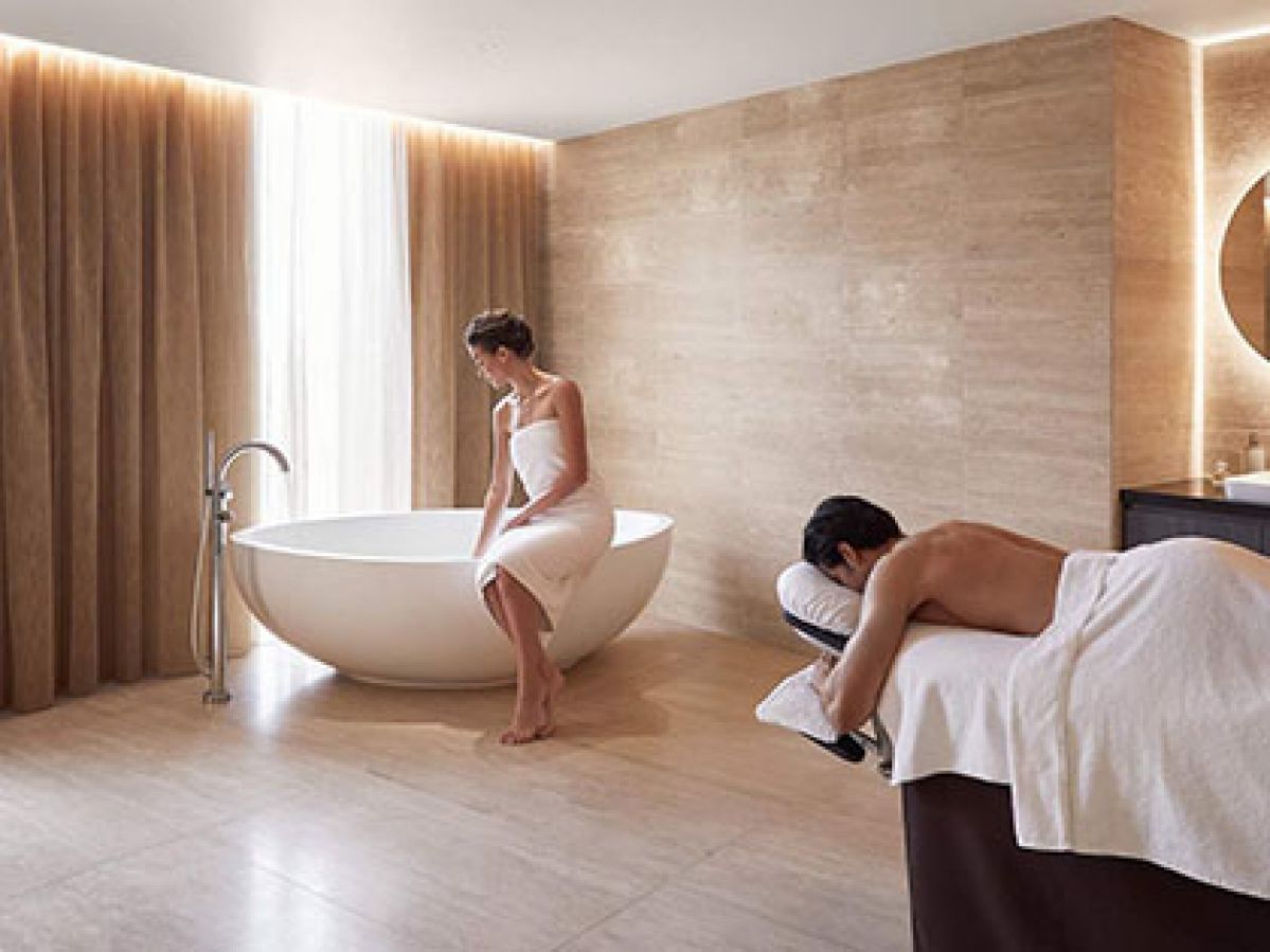 Couple enjoying treatment at RACV One Spa, woman filling a bath while man lies on a massage table.