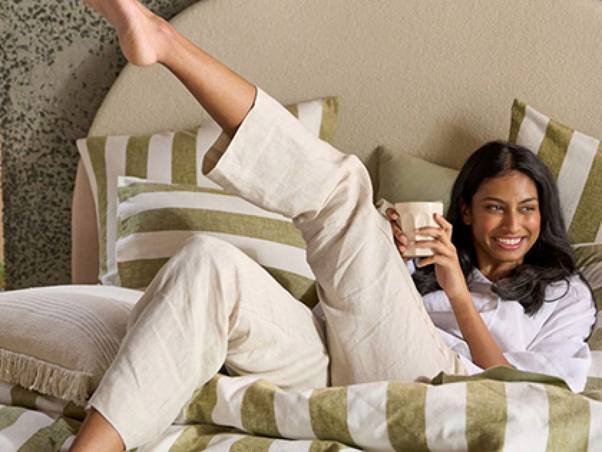 Smiling woman drinking coffee in bed on striped linen.
