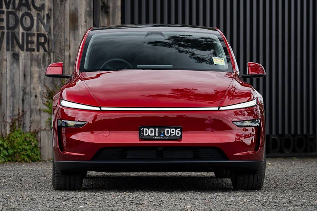 Red Tesla Model Y SUV parked in front of Mt Macedon winery building with grey weathered boards and black steel door.