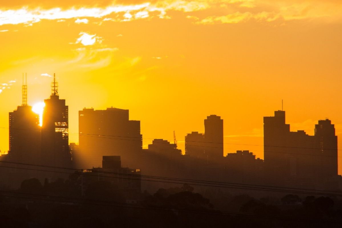 A large yellow sun setting behind the Melbourne city skyline, lighting up the sky in bright orange after a hot day