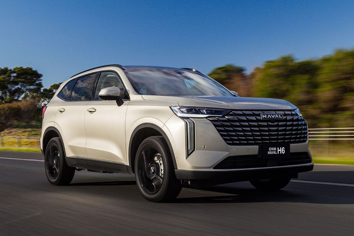 Pearl-coloured GWM Haval H6 plug-in hybrid SUV on dual-lane highway in country Victoria with trees and blue sky behind.