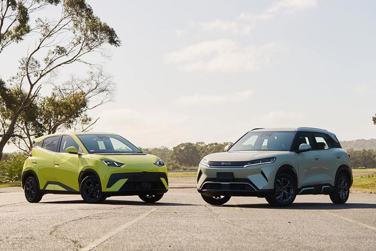 Yellow BYD Atto 1 hatch and cream-coloured BYD Atto 2 SUV parked at Lang Lang proving ground with gum trees behind. 