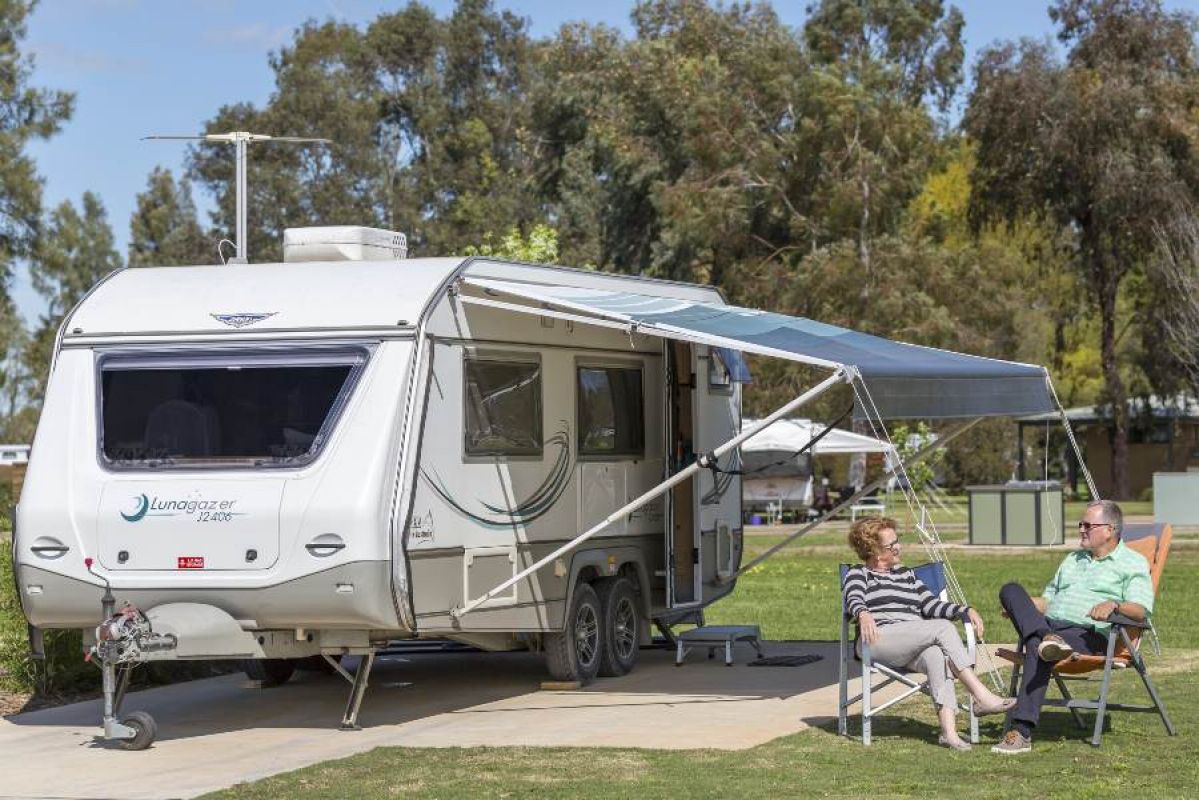 Two people sitting on camp chairs next to a caravan in a caravan park