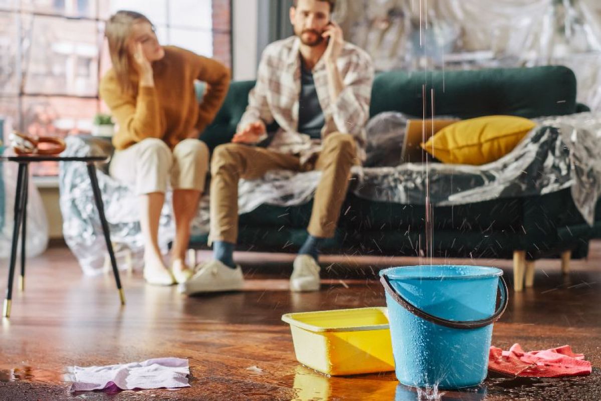 A water leak in the roof dripping into a blue bucket in an apartment