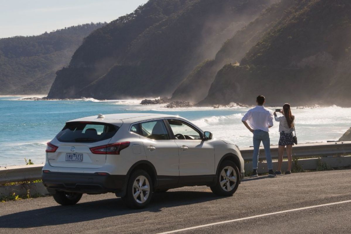 A couple admiring the ocean from the Great Ocean Road while their white SUV car is parked nearby