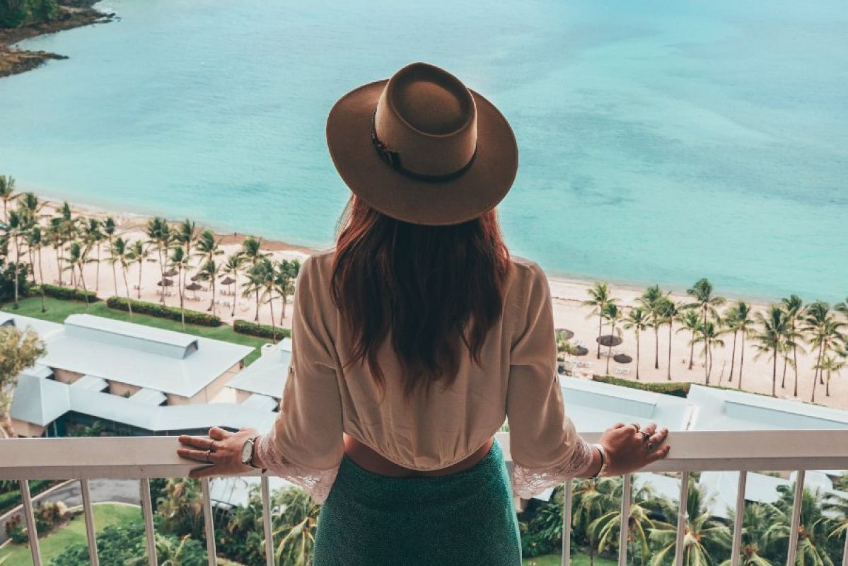 woman standing on hotel balcony looking at tropical beach