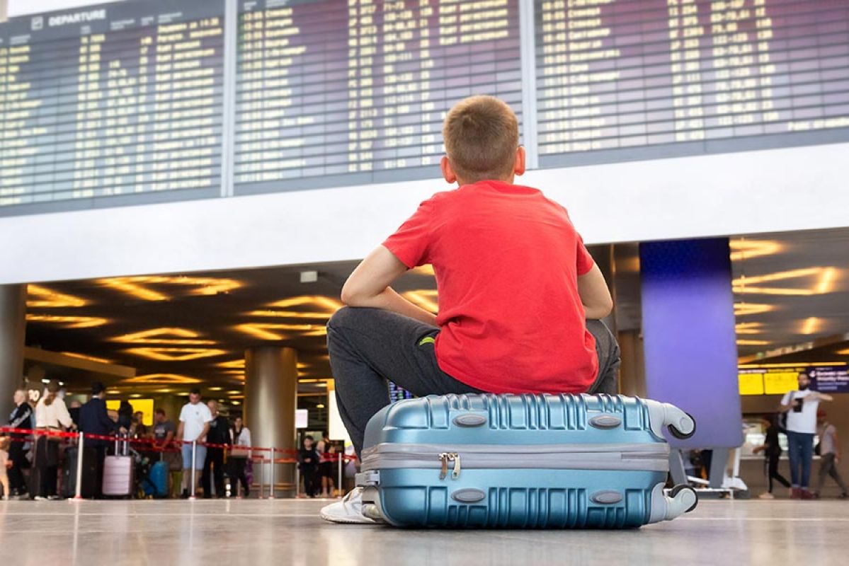 Boy sitting on suitcase at airport looking up at departures board