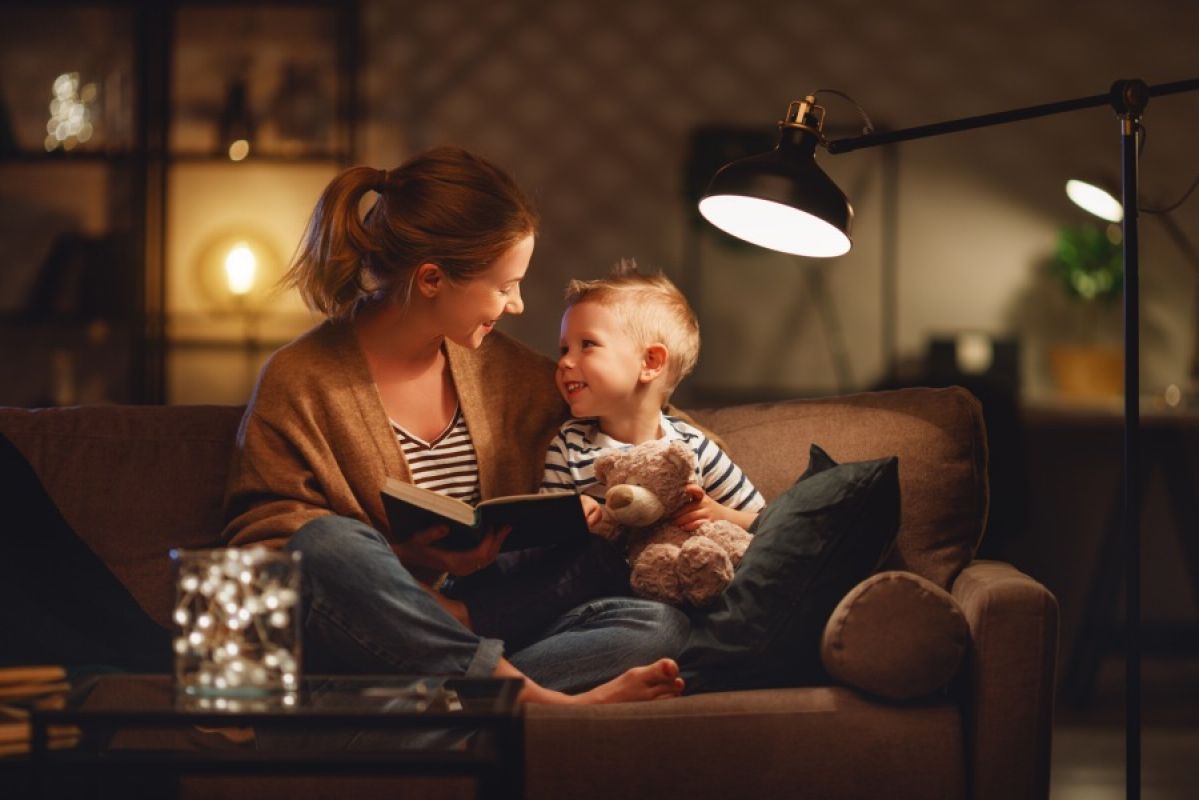 woman and child reading a book on couch under a lamp
