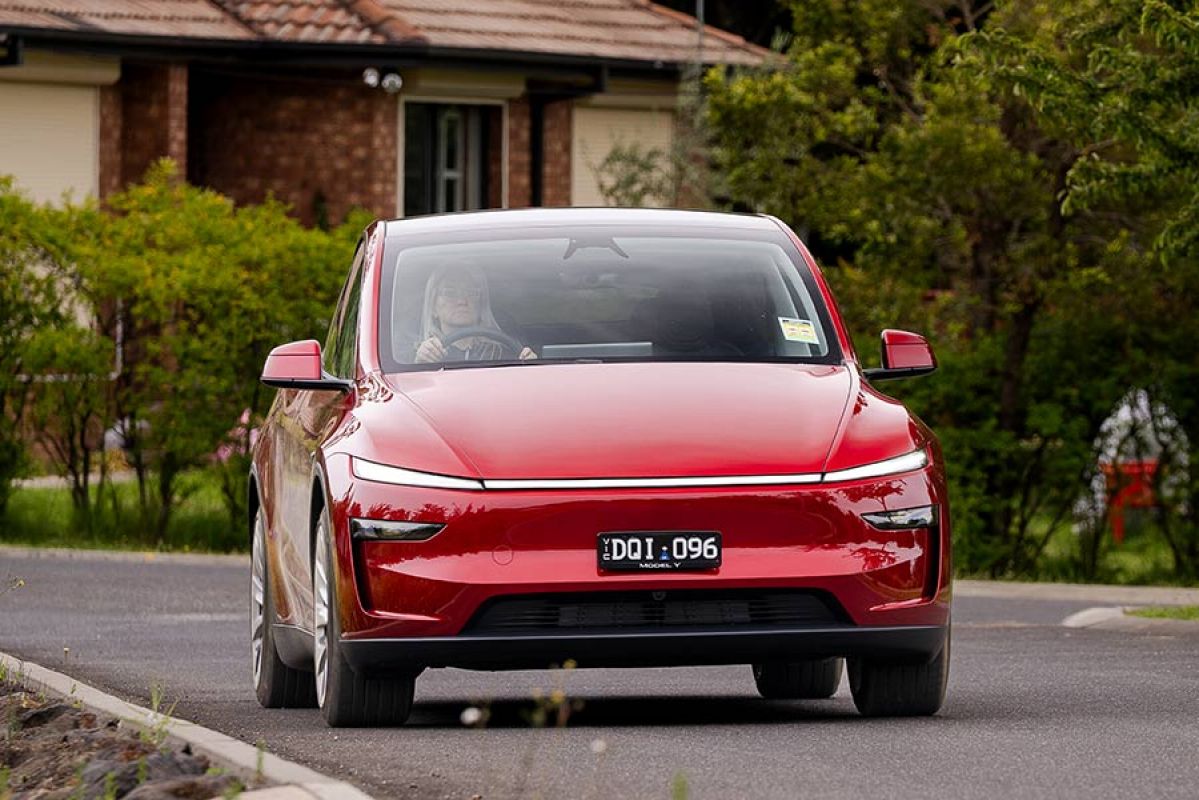 Red Tesla Model Y SUV on leafy suburban street with RACV motoring editor Andrea Matthews behind the wheel.