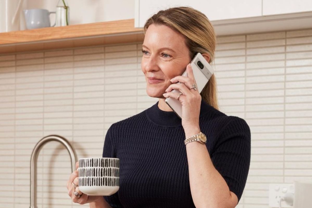 A woman smiling while using a mobile phone  in a kitchen