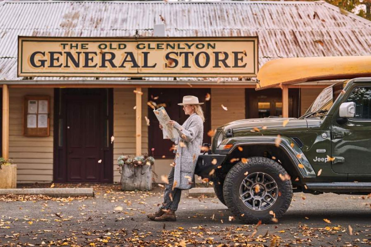 woman looking at paper leaning against a green jeep outside a country general store