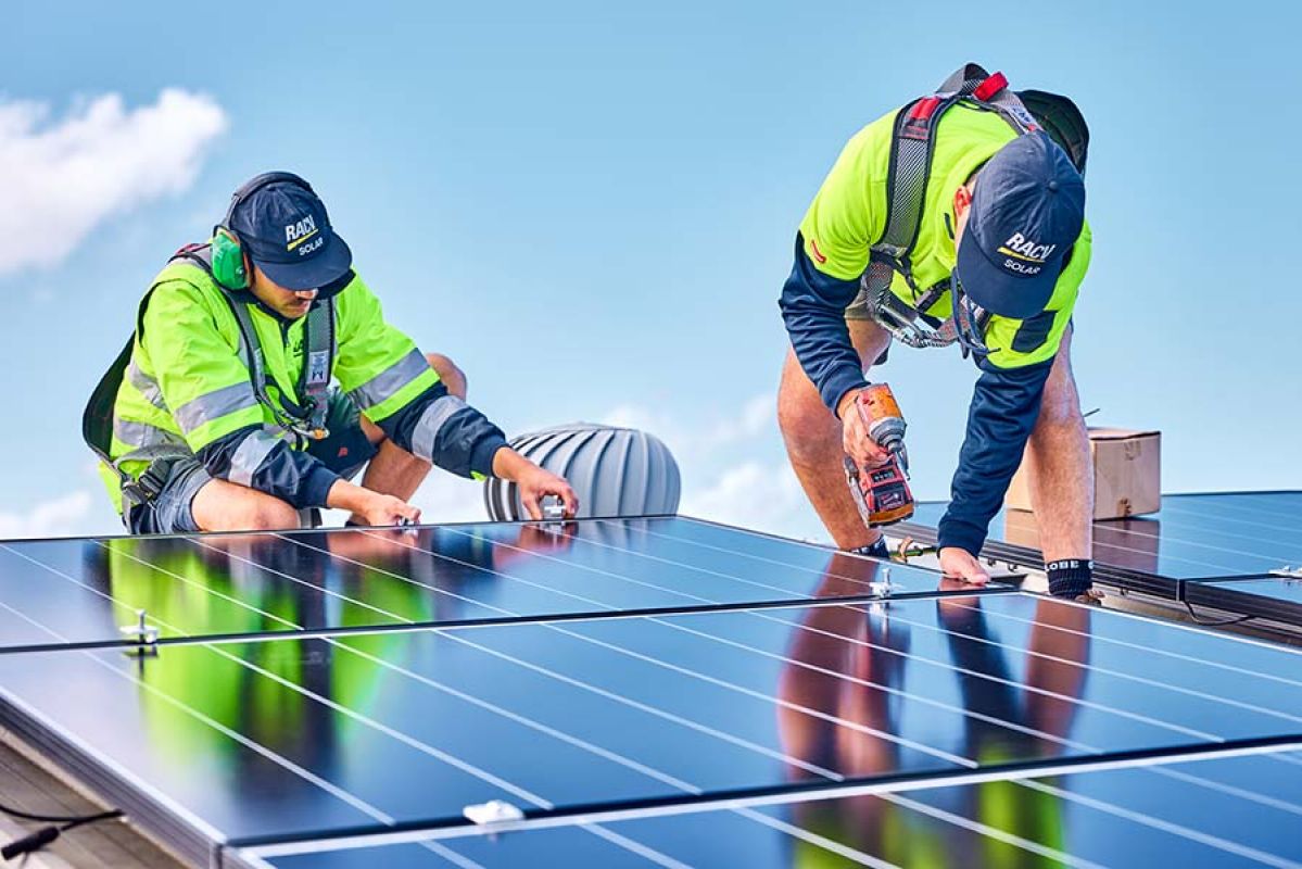 Two tradies wearing hi-vis clothing installing a solar panel on a roof