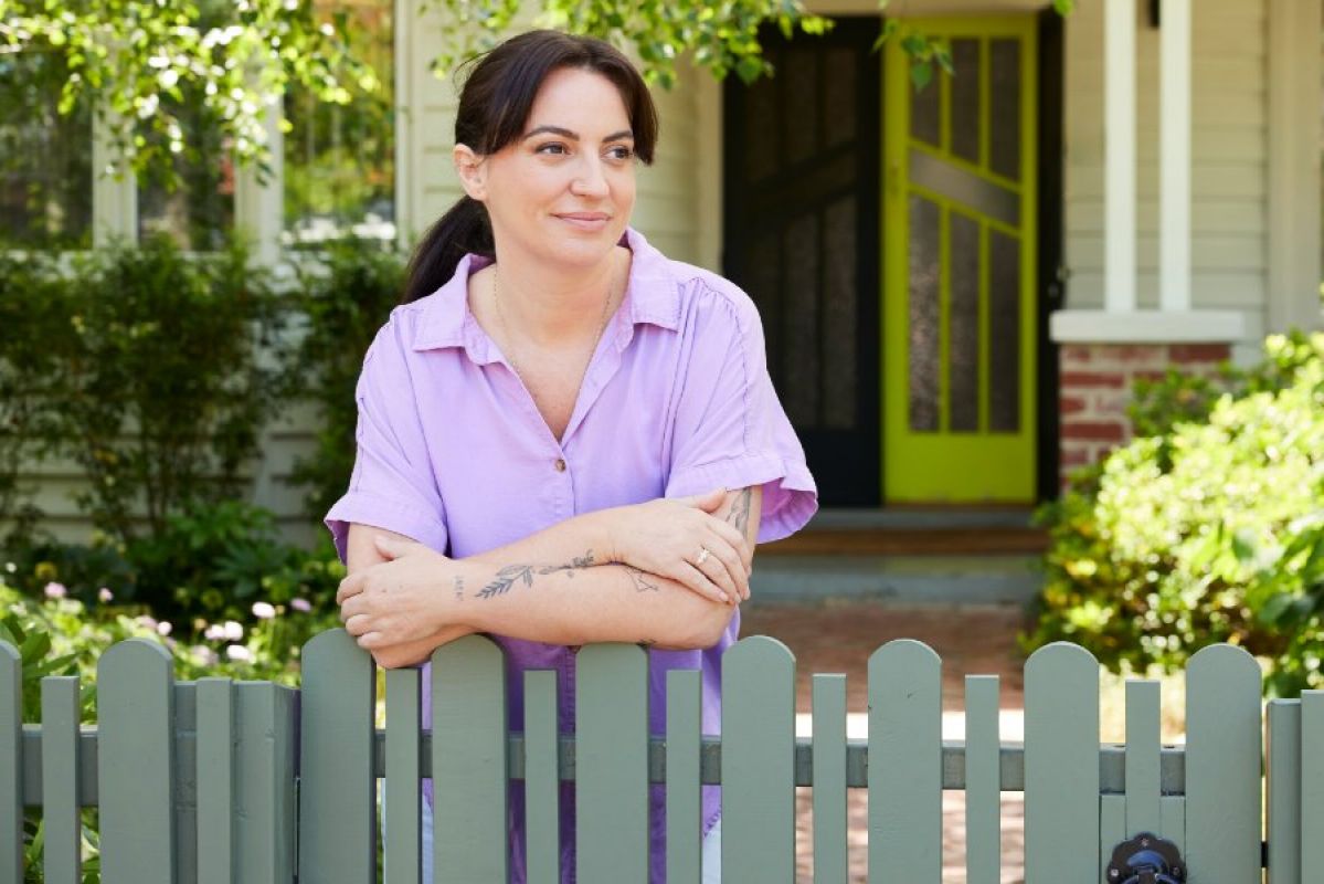 young woman leaning on fence in front of her house