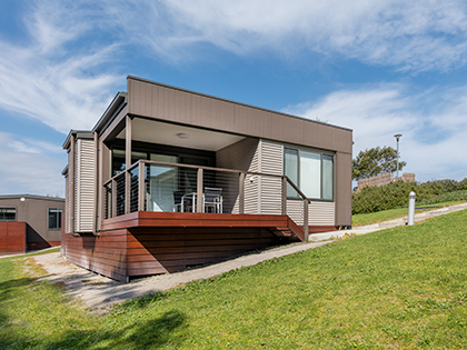 Deluxe Twin Cabin set on a hill at RACV Inverloch Resort, featuring a wooden verandah with tables and chairs.