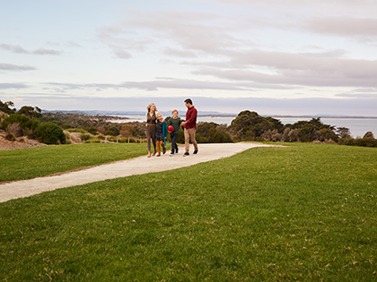 Parents and two kids walking along a path near RACV Inverloch Resort, with the beach behind them.