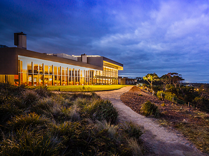 Path surrounded by greenery leading to the main RACV Inverloch Resort building, lit up at night.