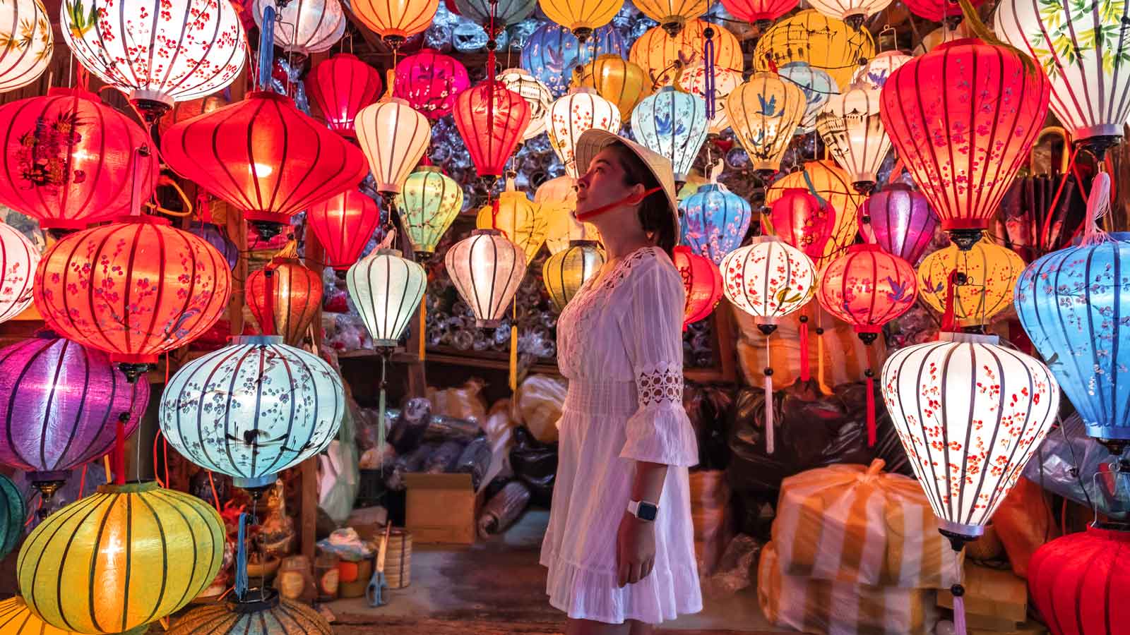 A woman wearing a rice hat in a shop admiring the colorful lanterns. 