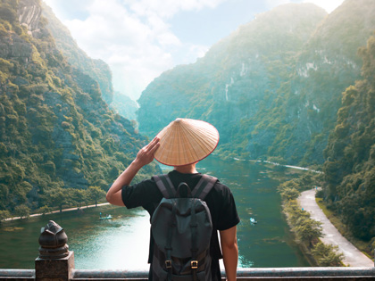 Man overlooking river and mountains wearing Vietnamese hat