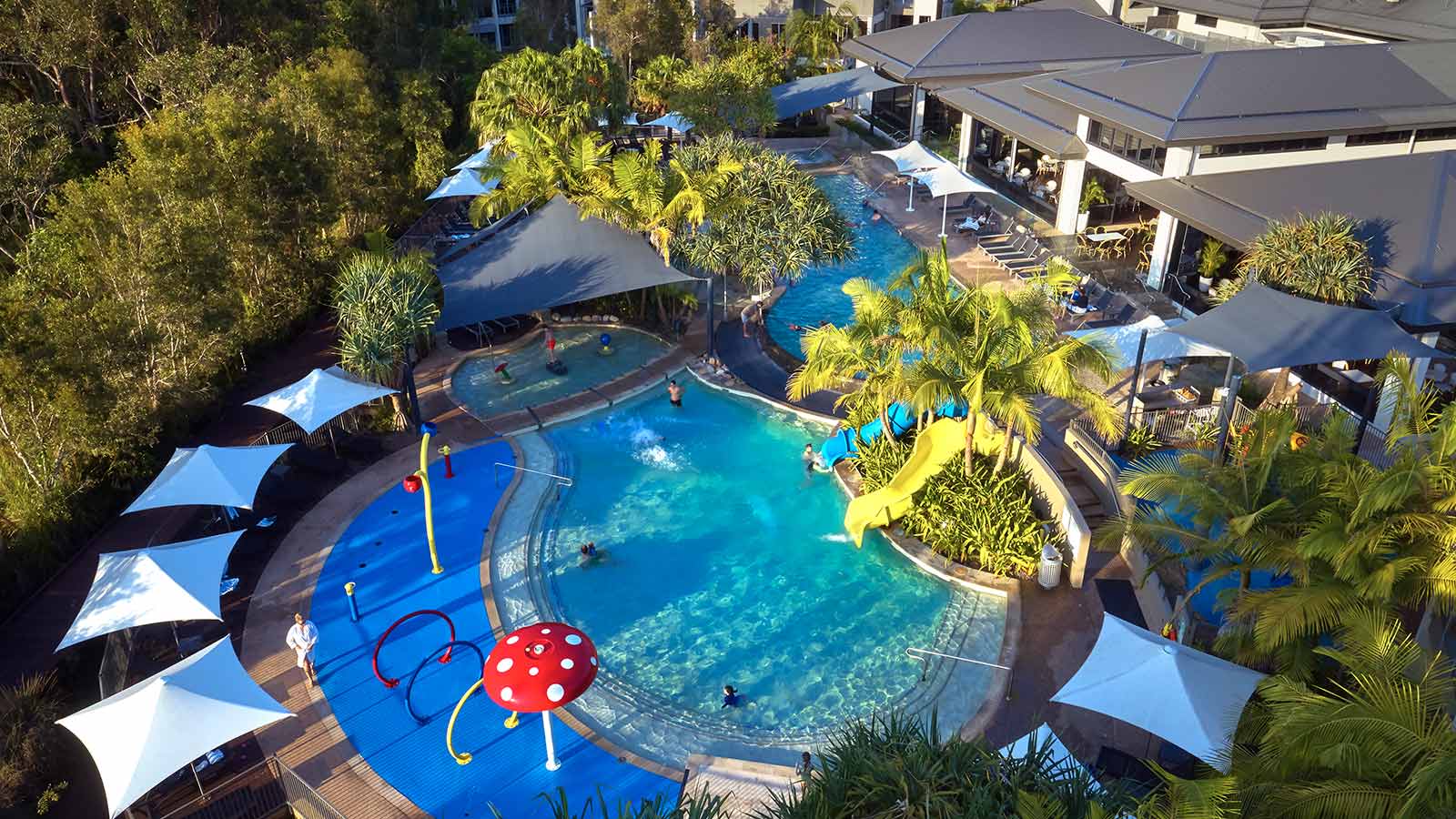 RACV Noosa Resort's pool, surrounded by trees and white umbrellas.