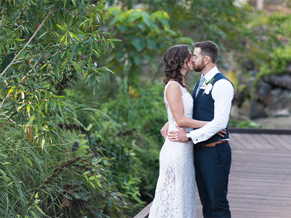 Bride and groom kissing on a deck at the Noosa Resort, surrounded by greenery.
