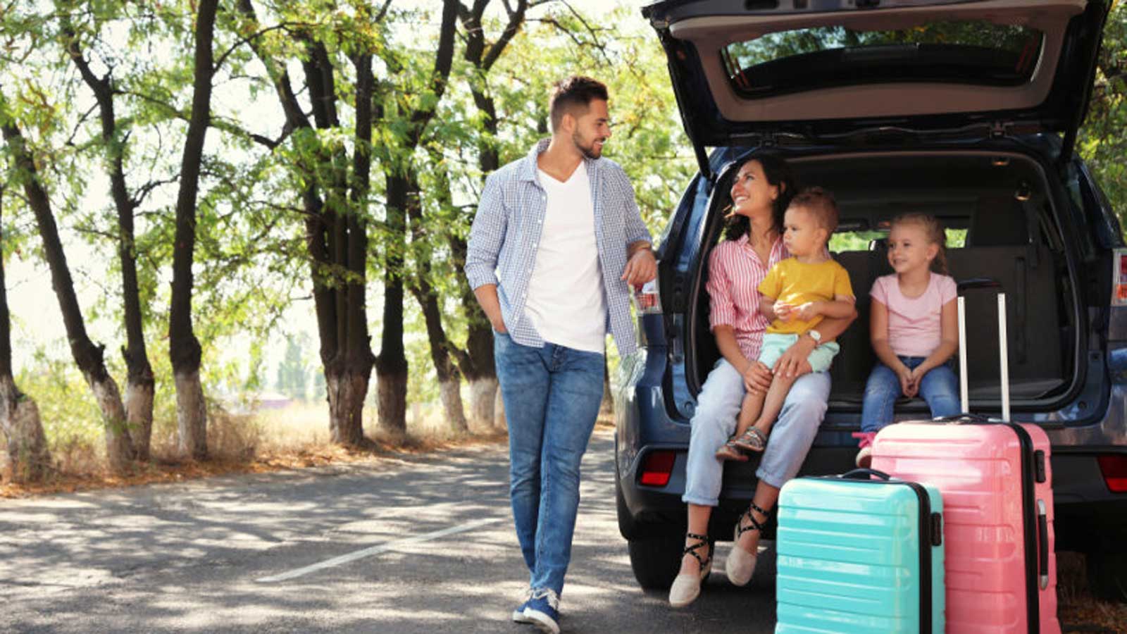 A travelling young family parked on the side of a shaded road with their suitcases